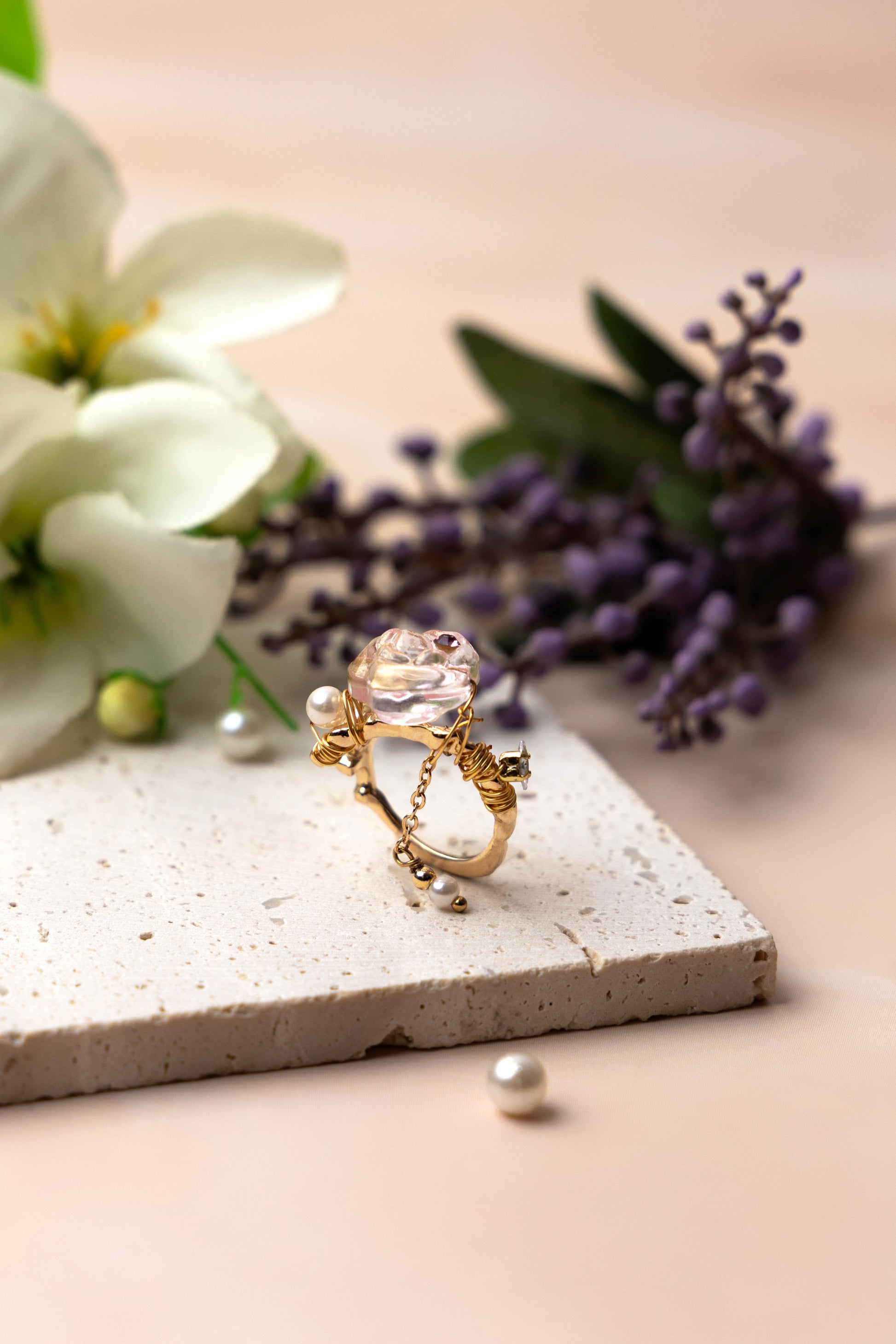 A handcrafted ring with a crystal-like floral centerpiece and an elegant coiled band, featuring a delicate hanging chain with a pearl-like drop that adds graceful movement and distinctive cha