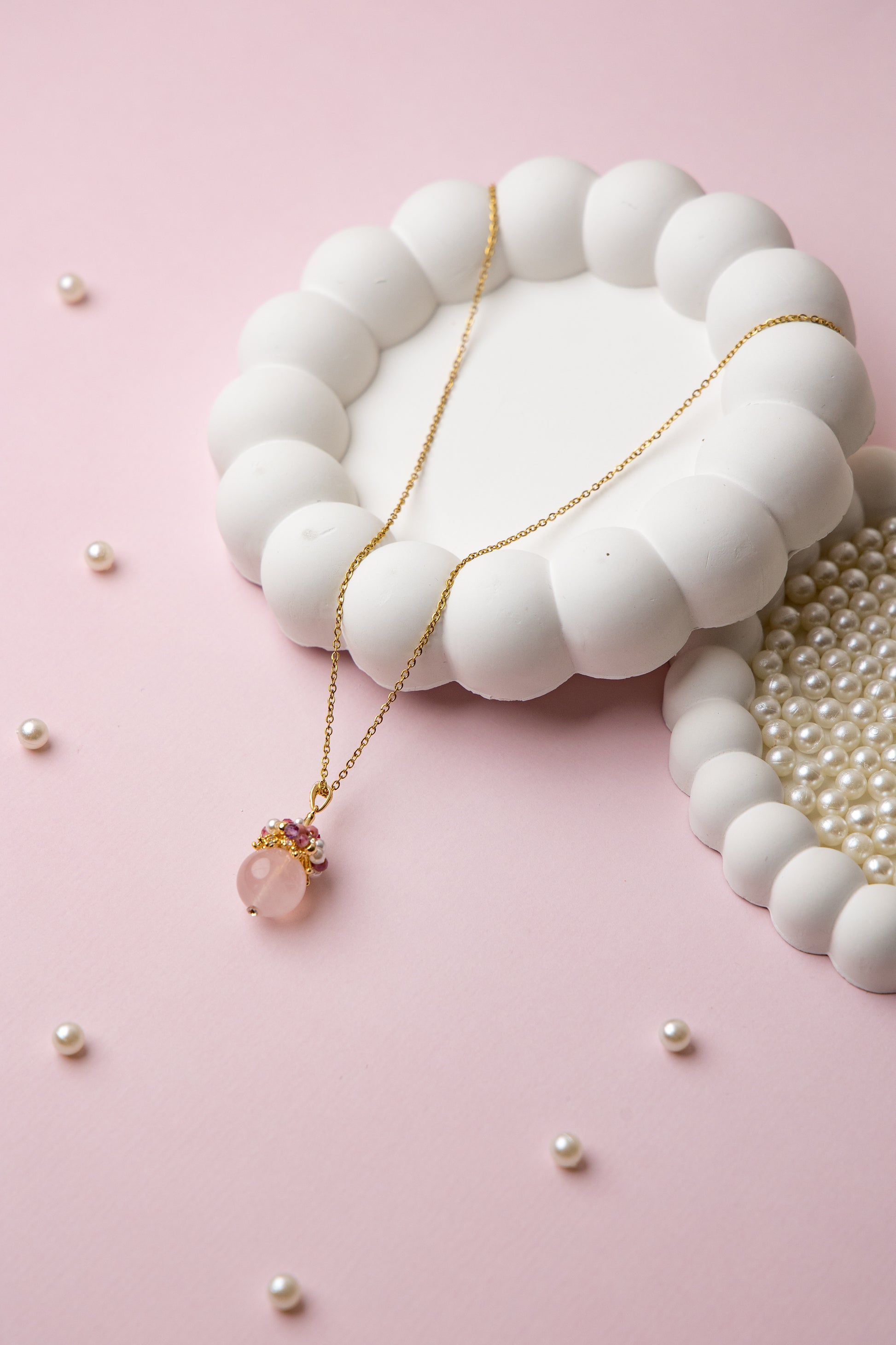 Close-up of an elegant necklace featuring a soft pink rose quartz orb, accented with a cluster of luminous freshwater pearls and deep pink tourmaline beads, evoking charm, femininity, and grace.