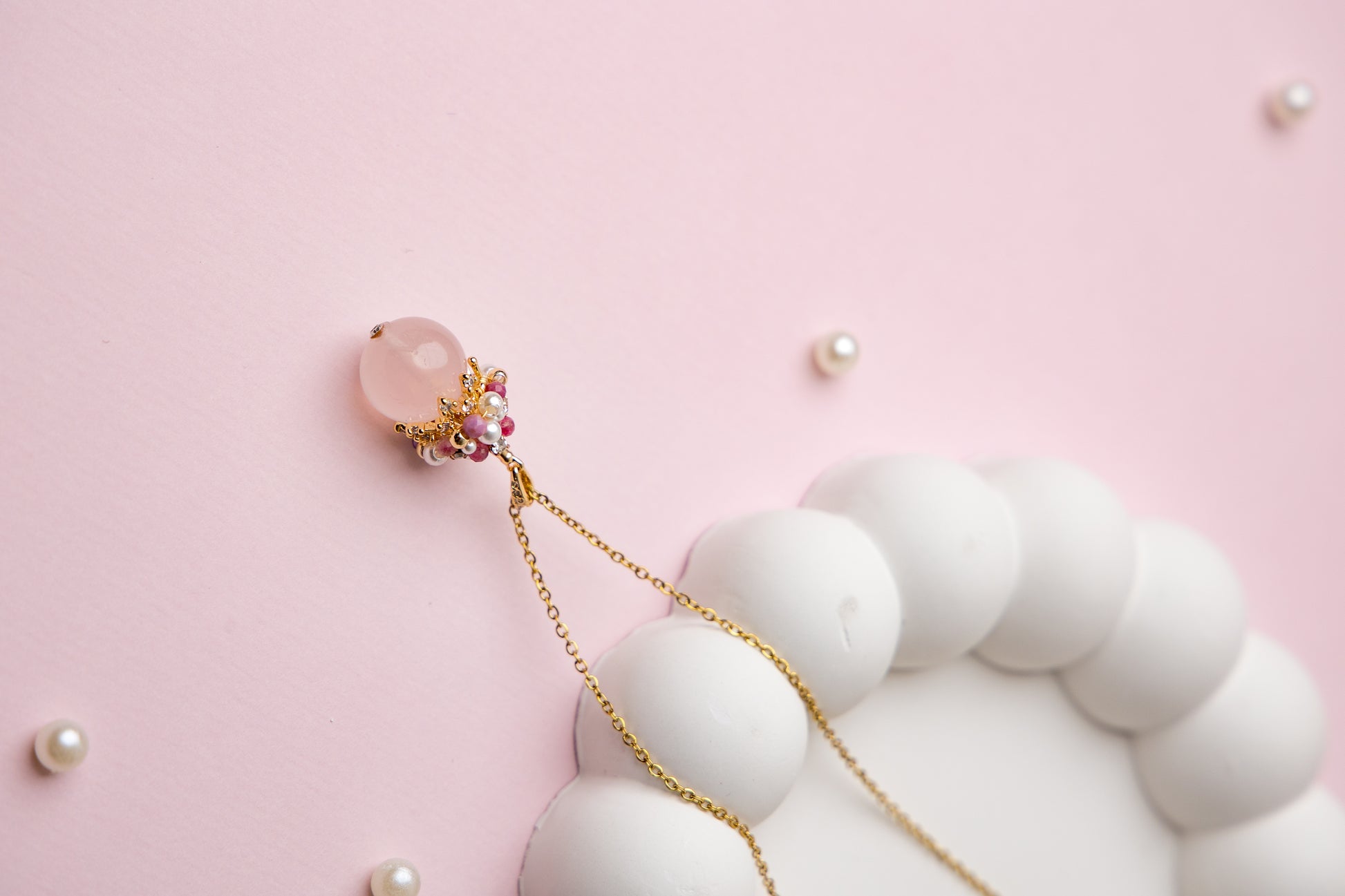 Close-up of an elegant necklace featuring a soft pink rose quartz orb, accented with a cluster of luminous freshwater pearls and deep pink tourmaline beads, evoking charm, femininity, and grace.