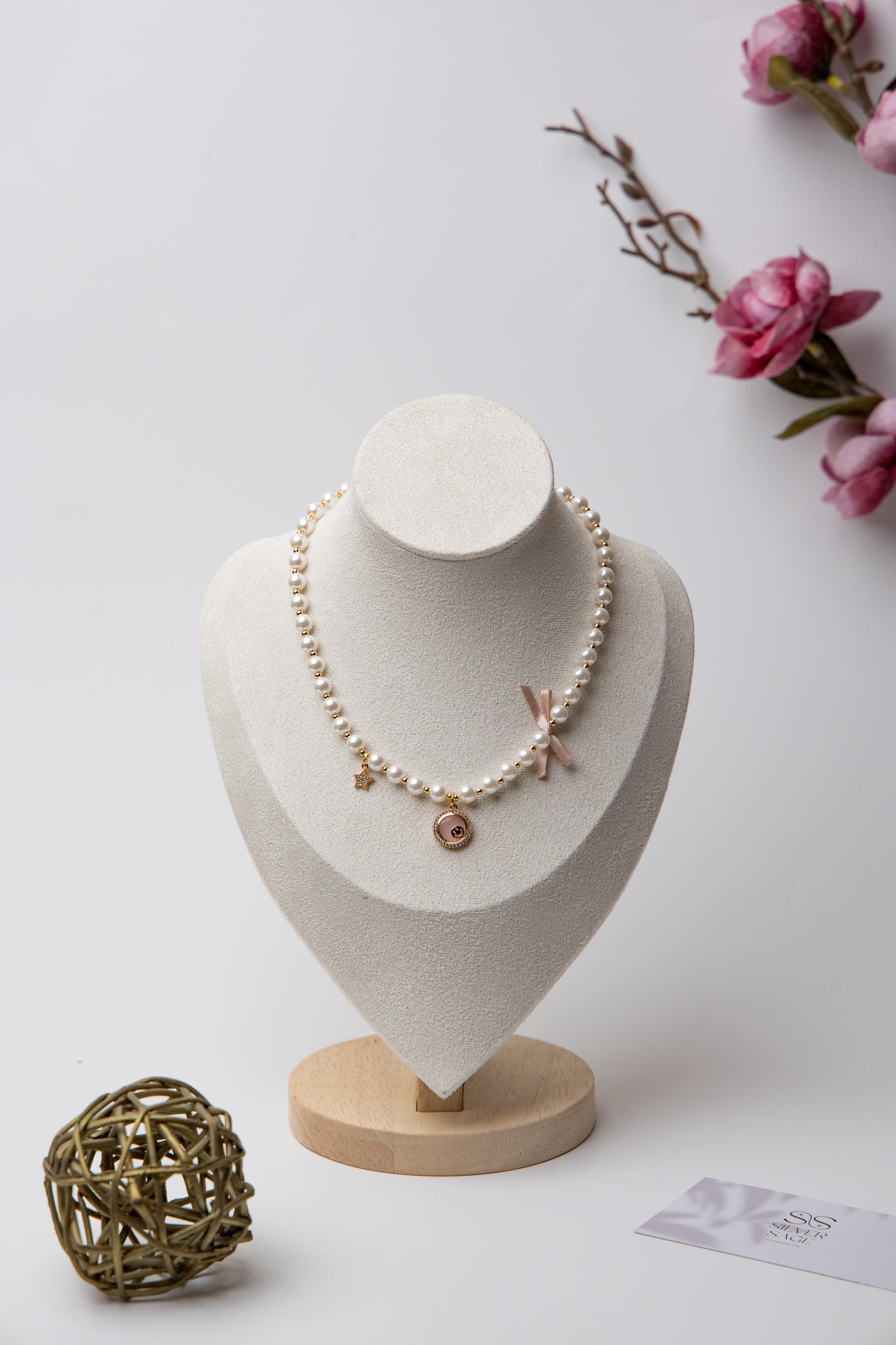 A romantic pearl necklace accented with a soft pink enamel rose charm and a satin bow. Feminine and perfect for gifting.