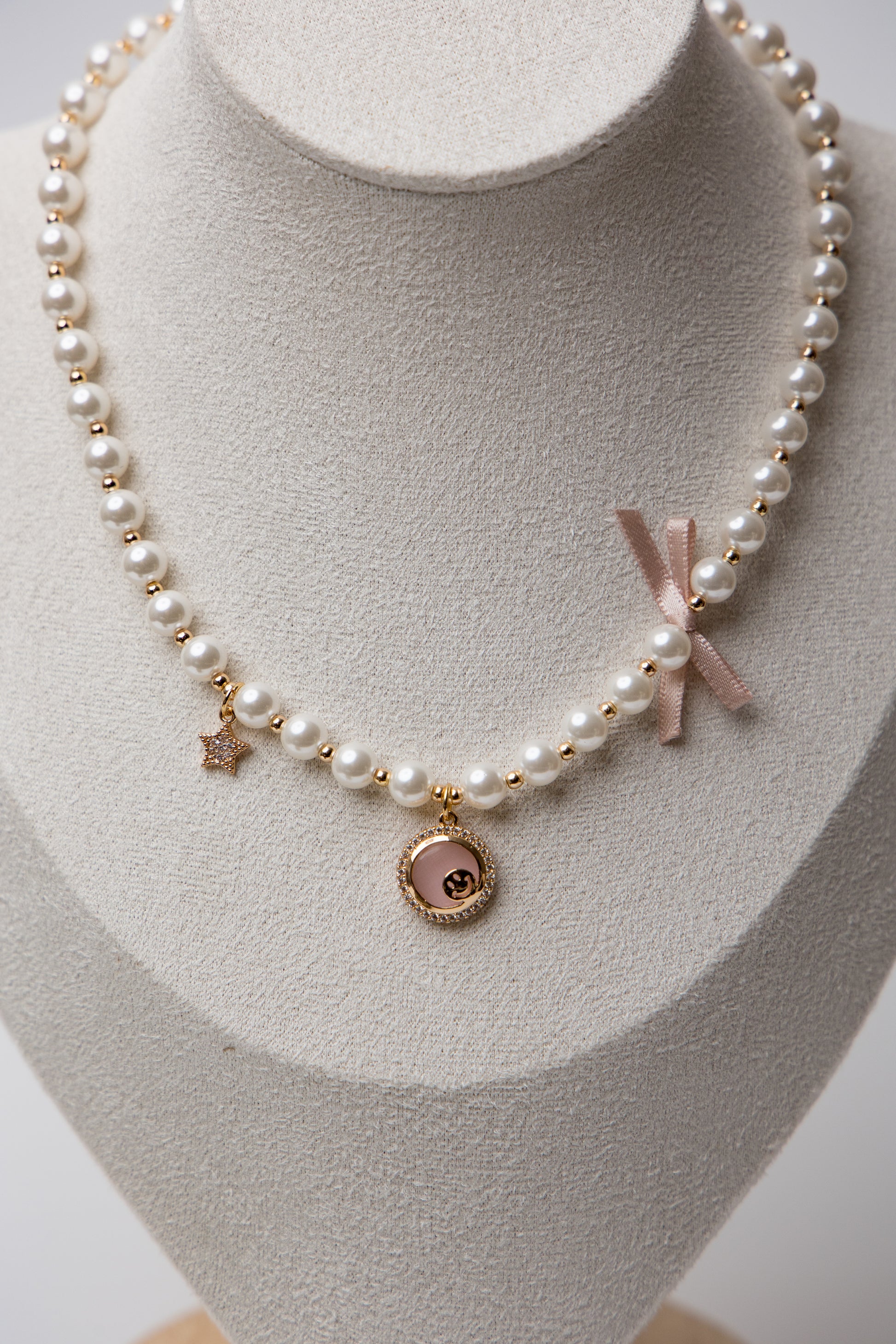 A romantic pearl necklace accented with a soft pink enamel rose charm and a satin bow. Feminine and perfect for gifting.