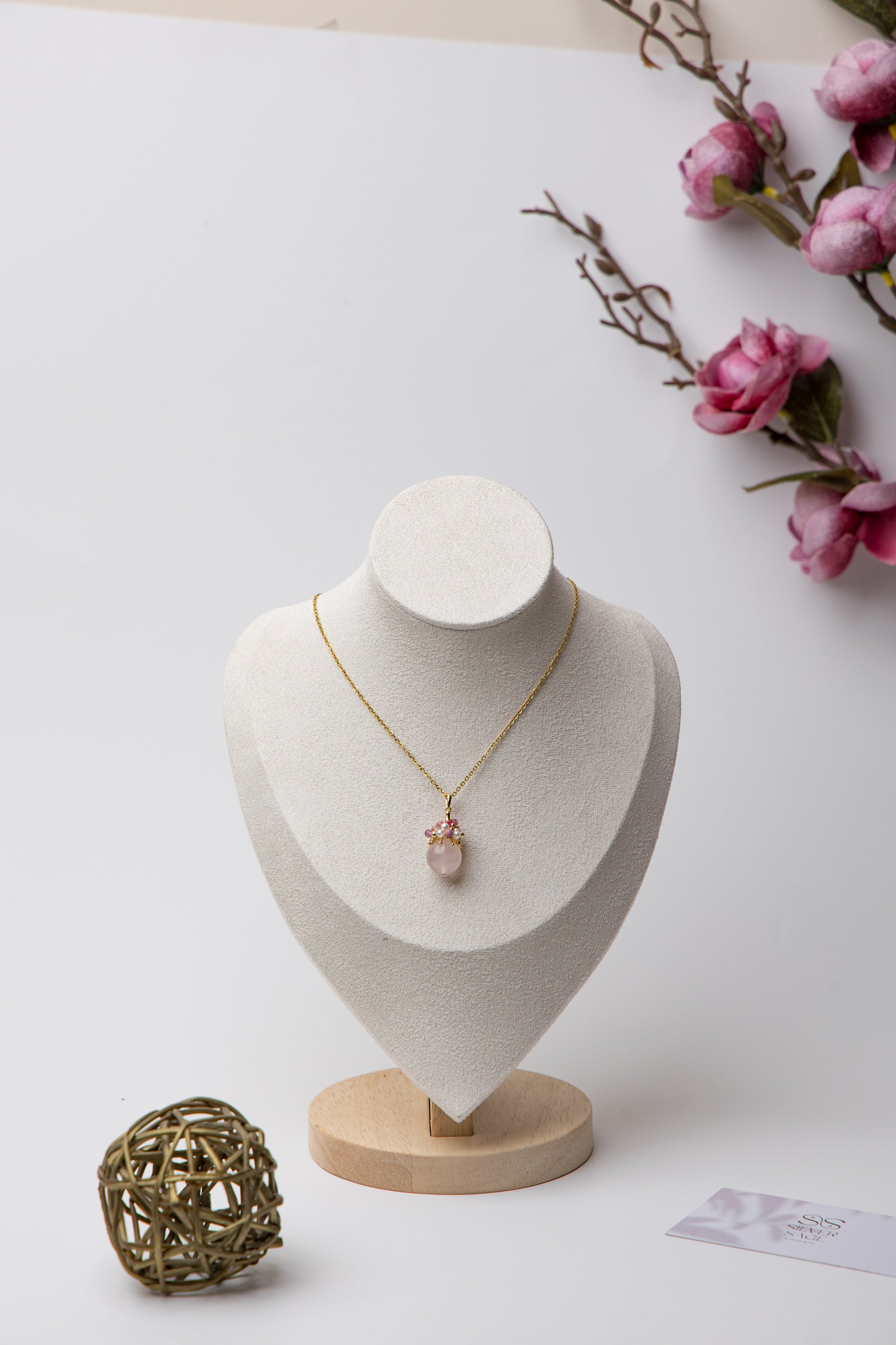 Close-up of an elegant necklace featuring a soft pink rose quartz orb, accented with a cluster of luminous freshwater pearls and deep pink tourmaline beads, evoking charm, femininity, and grace.