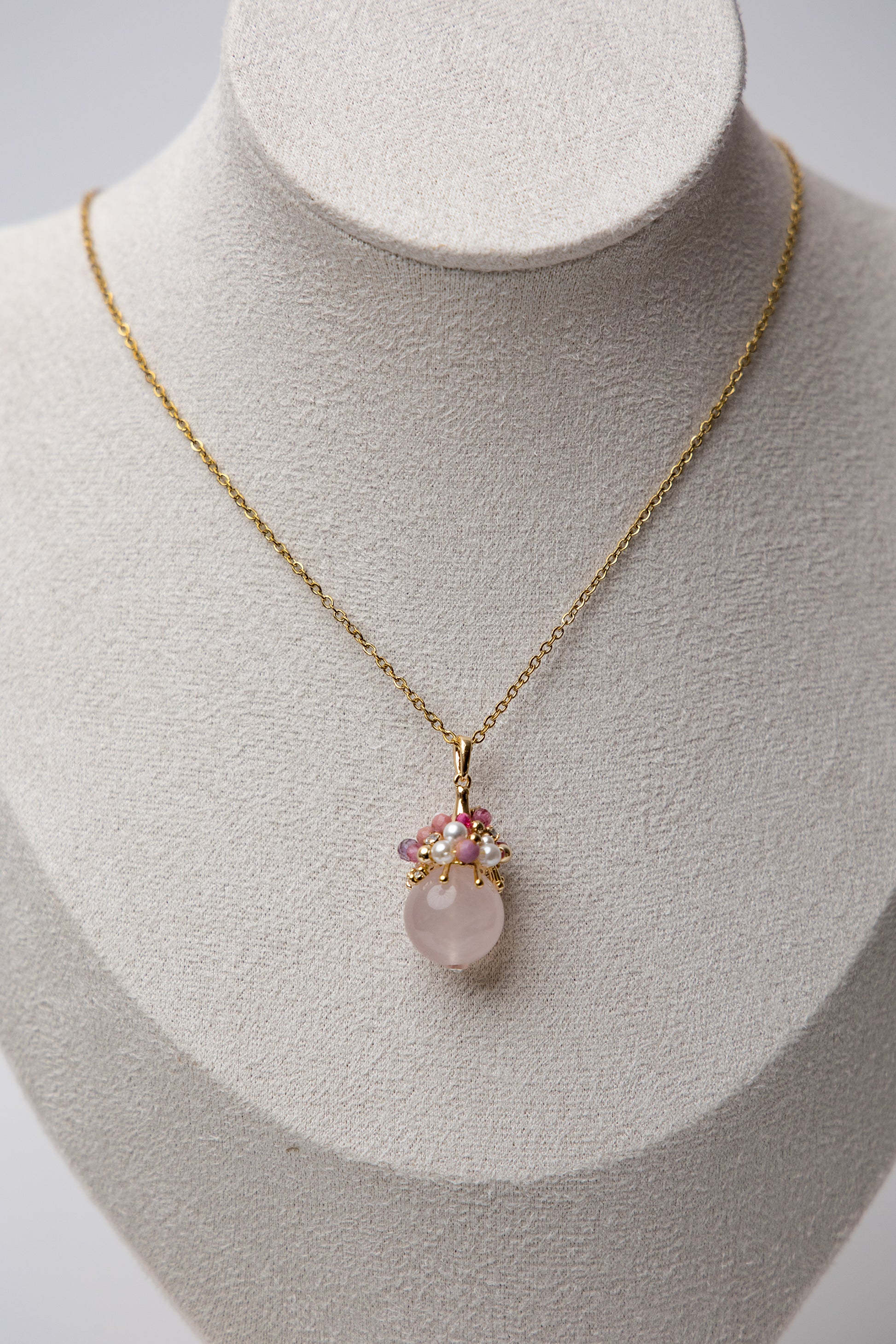 Close-up of an elegant necklace featuring a soft pink rose quartz orb, accented with a cluster of luminous freshwater pearls and deep pink tourmaline beads, evoking charm, femininity, and grace.