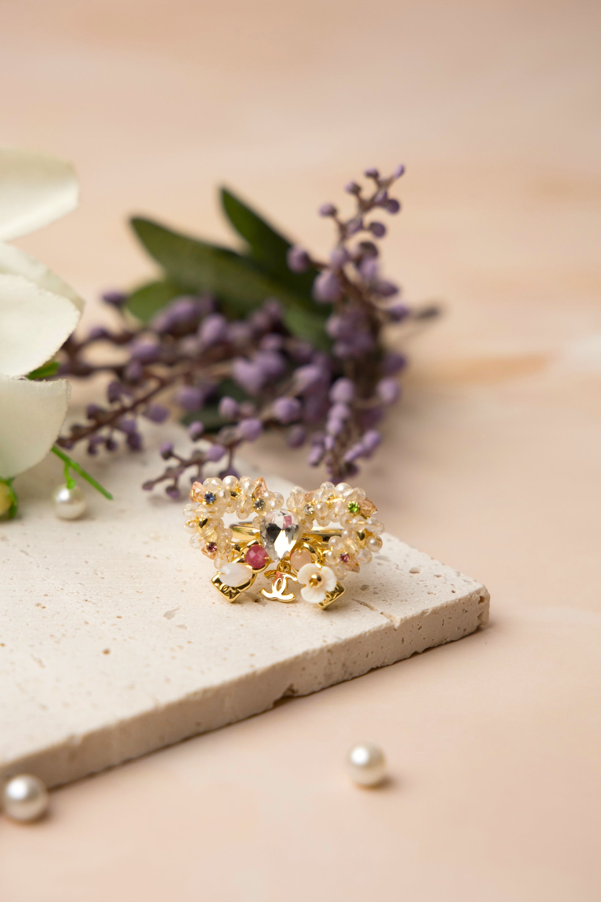 A delicately handcrafted gold-tone ring in the shape of a bow, adorned with clusters of luminous pearls, shimmering crystals, and soft pastel accents, showcasing feminine charm and exquisite artisanal detail.