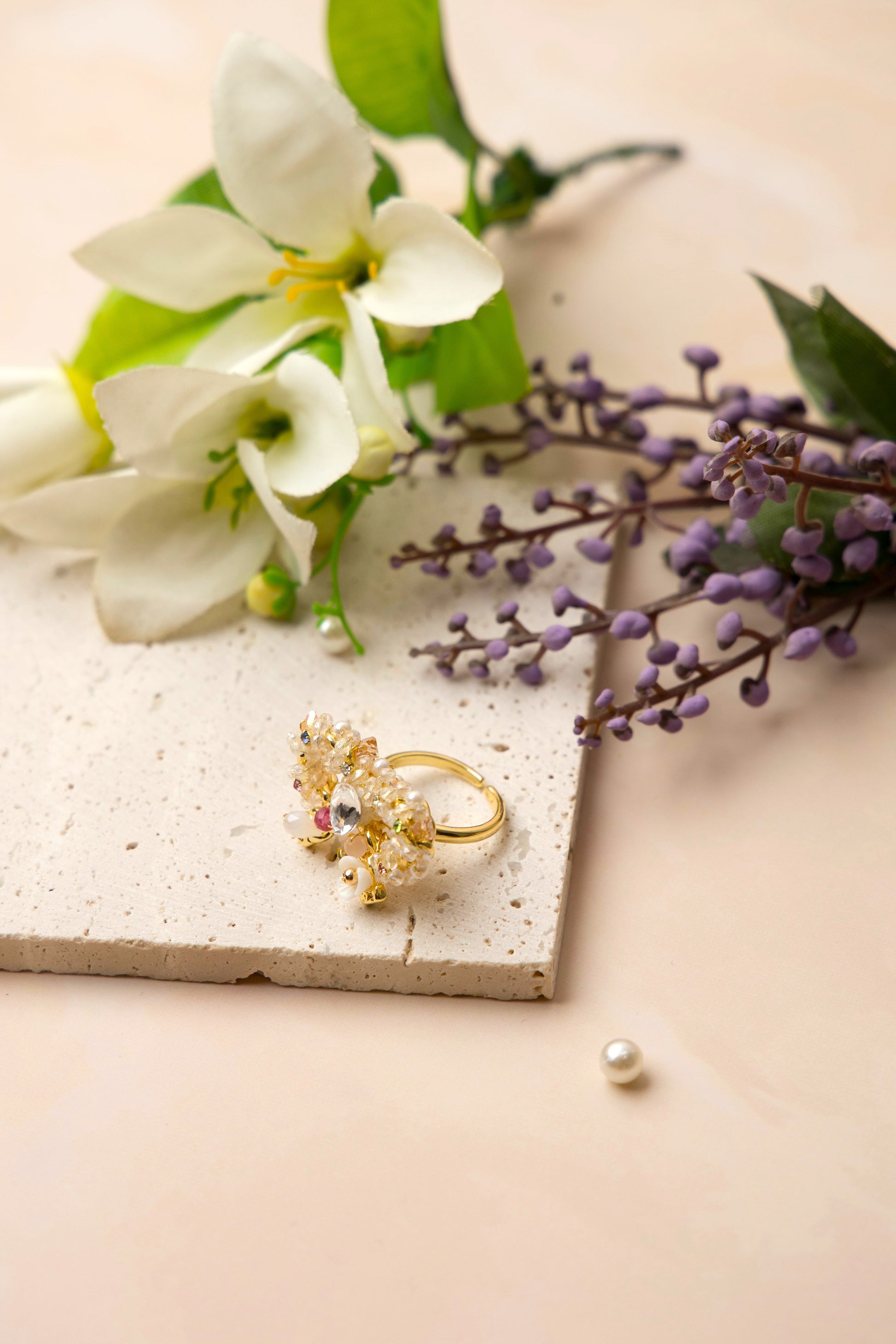 A delicately handcrafted gold-tone ring in the shape of a bow, adorned with clusters of luminous pearls, shimmering crystals, and soft pastel accents, showcasing feminine charm and exquisite artisanal detail.