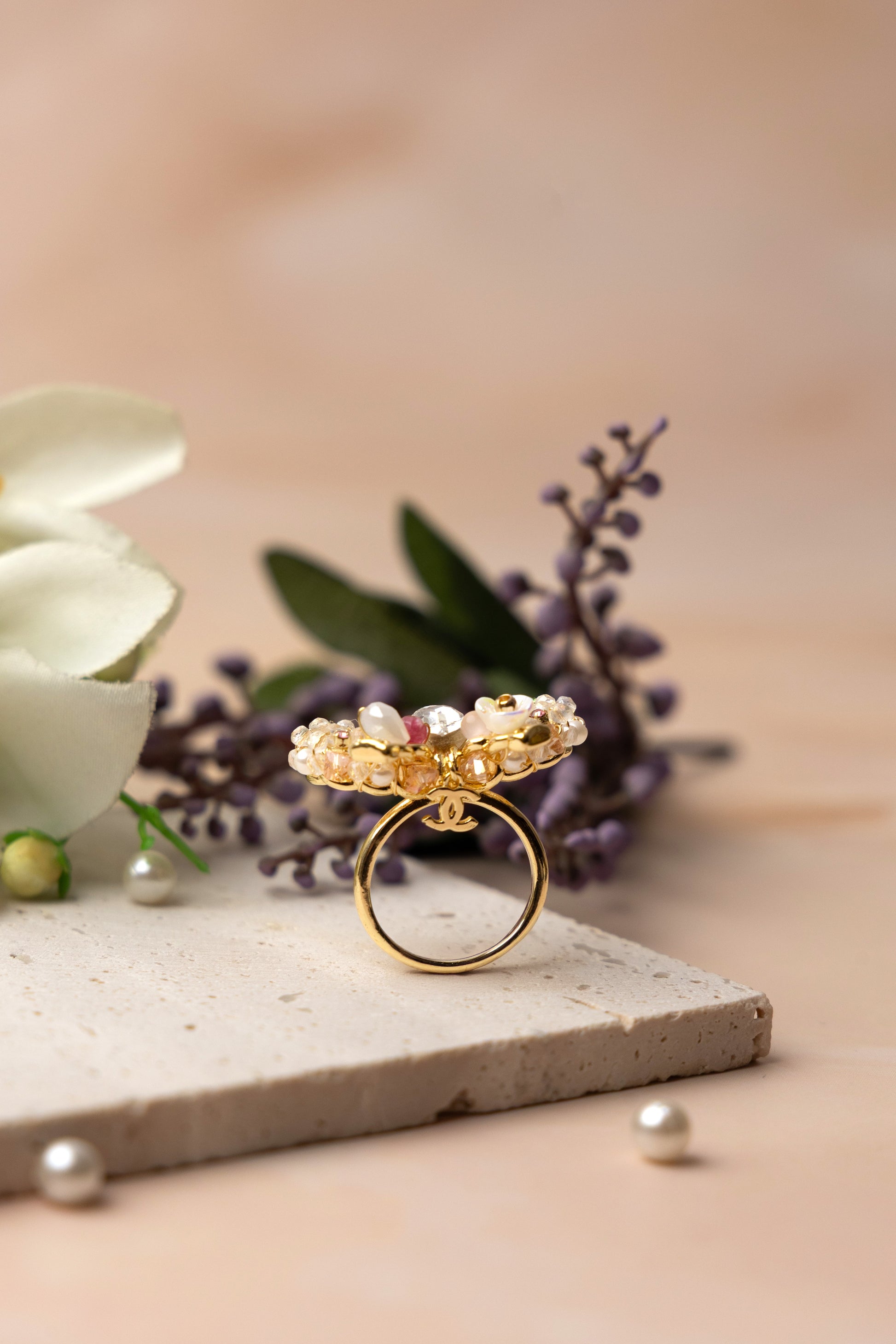 A delicately handcrafted gold-tone ring in the shape of a bow, adorned with clusters of luminous pearls, shimmering crystals, and soft pastel accents, showcasing feminine charm and exquisite artisanal detail.
