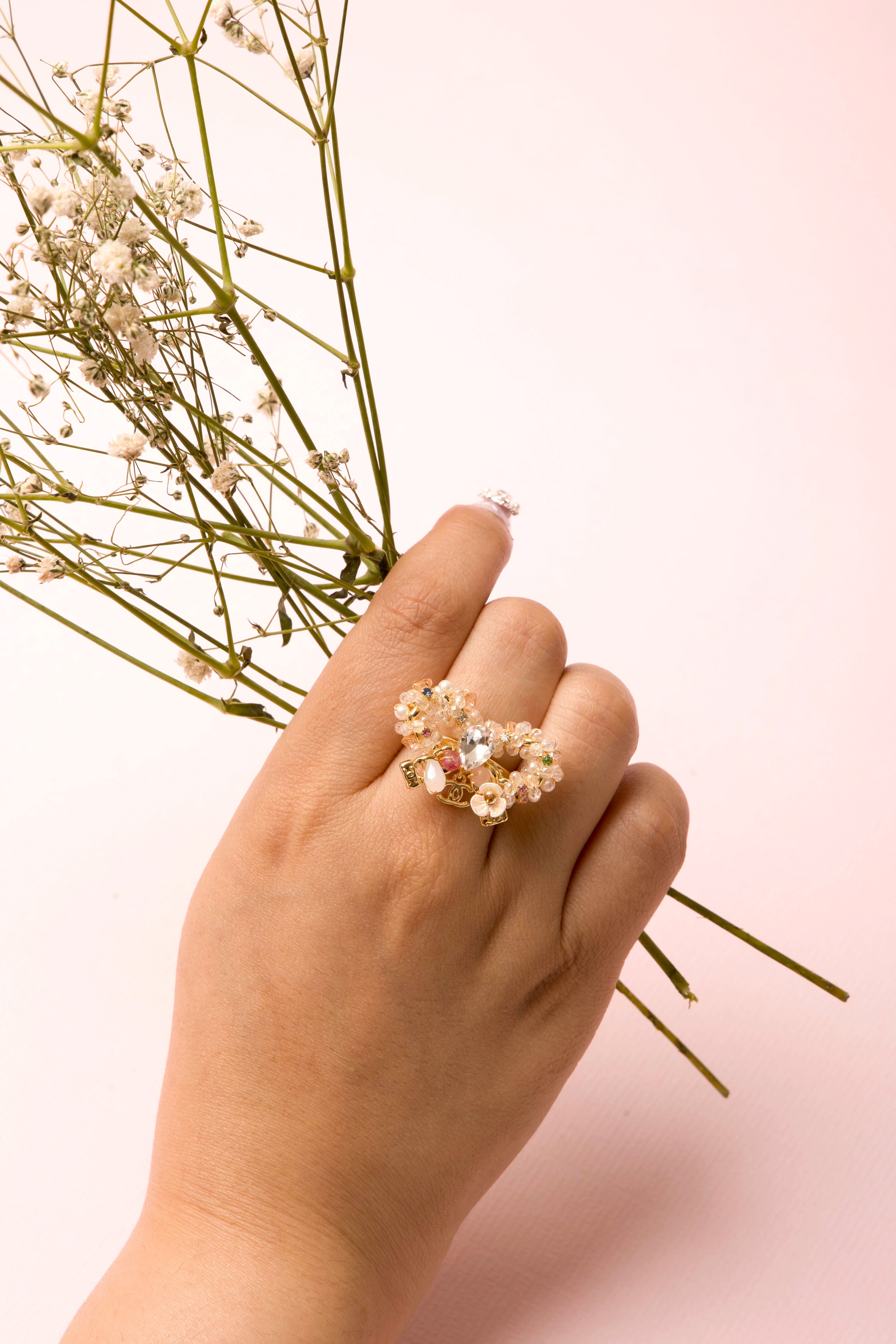 A delicately handcrafted gold-tone ring in the shape of a bow, adorned with clusters of luminous pearls, shimmering crystals, and soft pastel accents, showcasing feminine charm and exquisite artisanal detail.