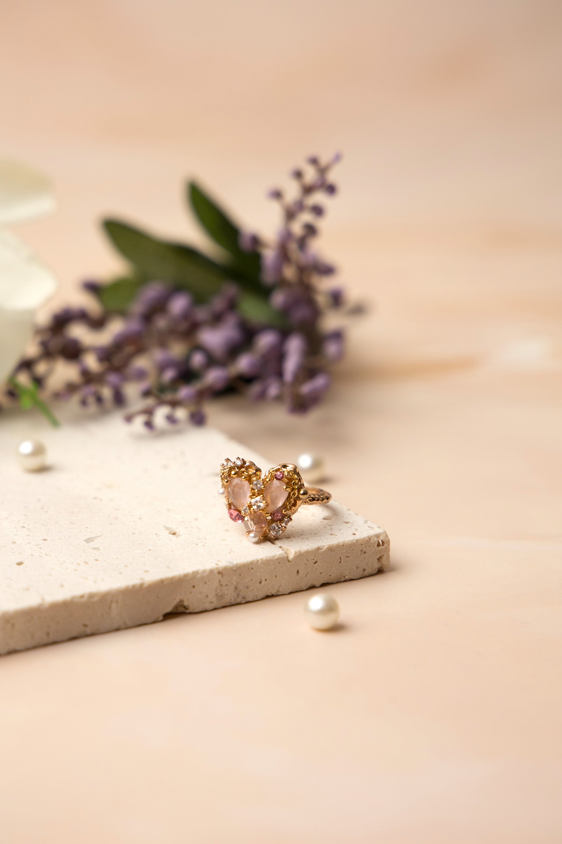 The Rosalind Heart Ring is crafted around a blushing heart-shaped crystal, encircled by dainty pearls and delicate stones.