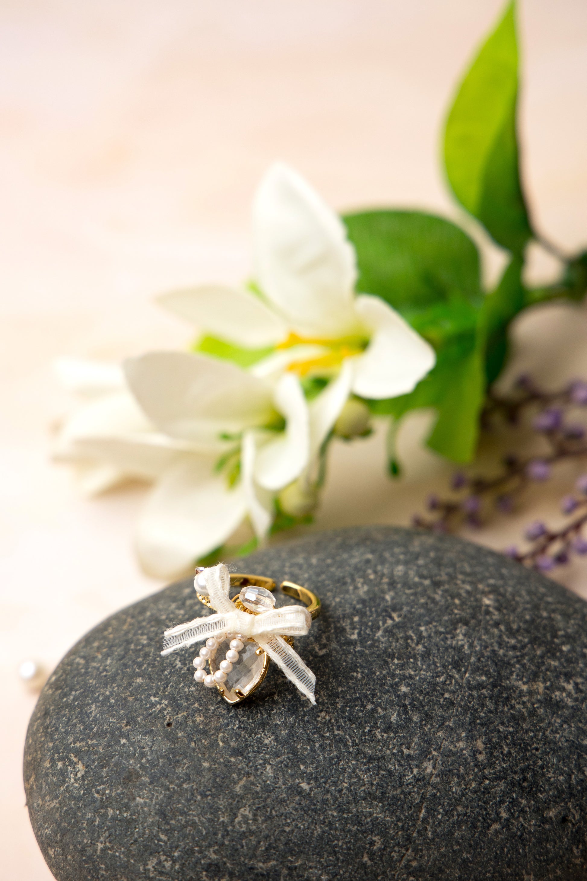 A romantic gold-tone ring showcasing a clear heart-shaped stone framed by tiny faux pearls in an arch, adorned with an ivory organza ribbon bow and a faceted bead for added sparkle and vintage charm.