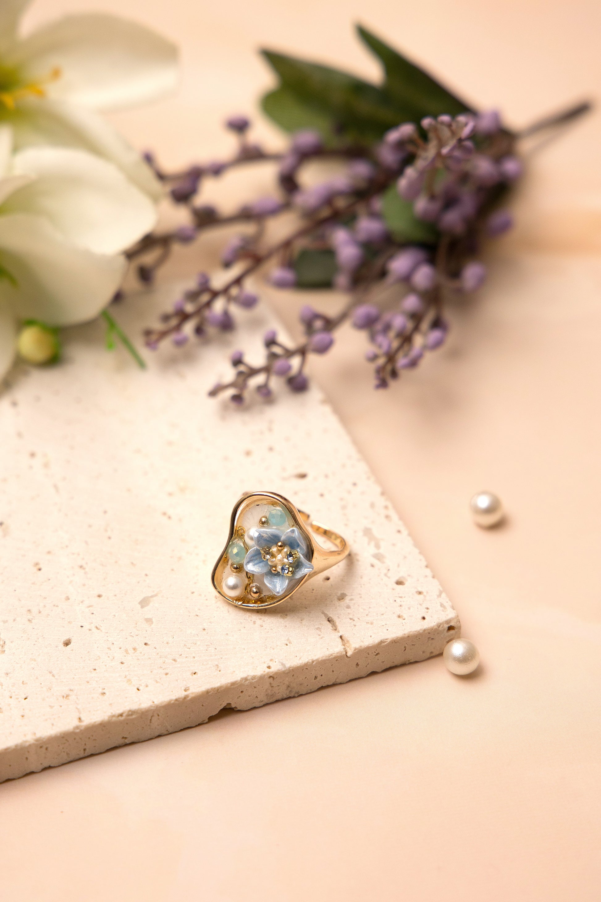 A gold-toned open band ring inspired by oceanic beauty, featuring a cluster of luminous pearls and a soft blue floral gem, arranged organically to resemble a hidden underwater treasure.