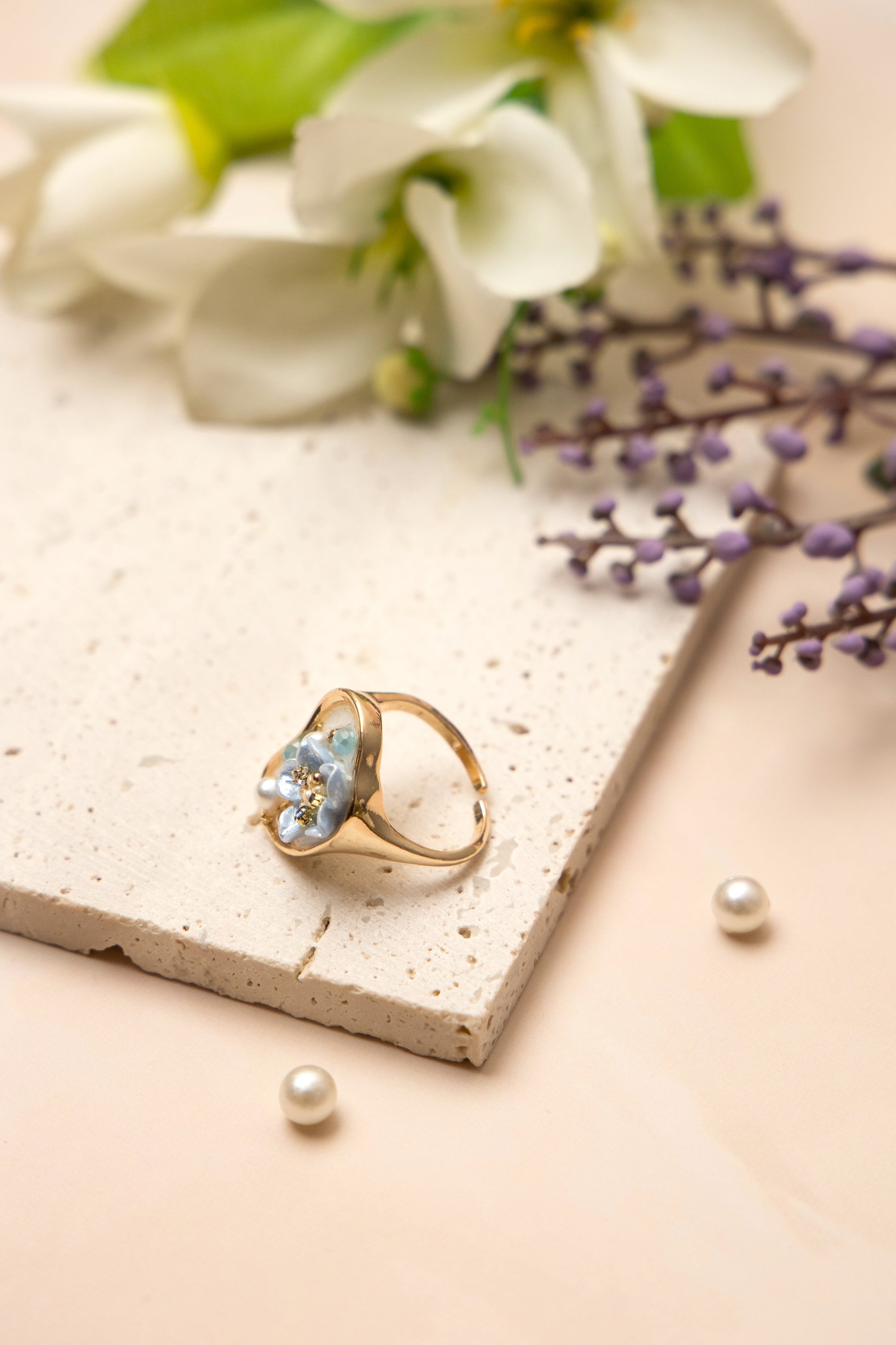 A gold-toned open band ring inspired by oceanic beauty, featuring a cluster of luminous pearls and a soft blue floral gem, arranged organically to resemble a hidden underwater treasure.