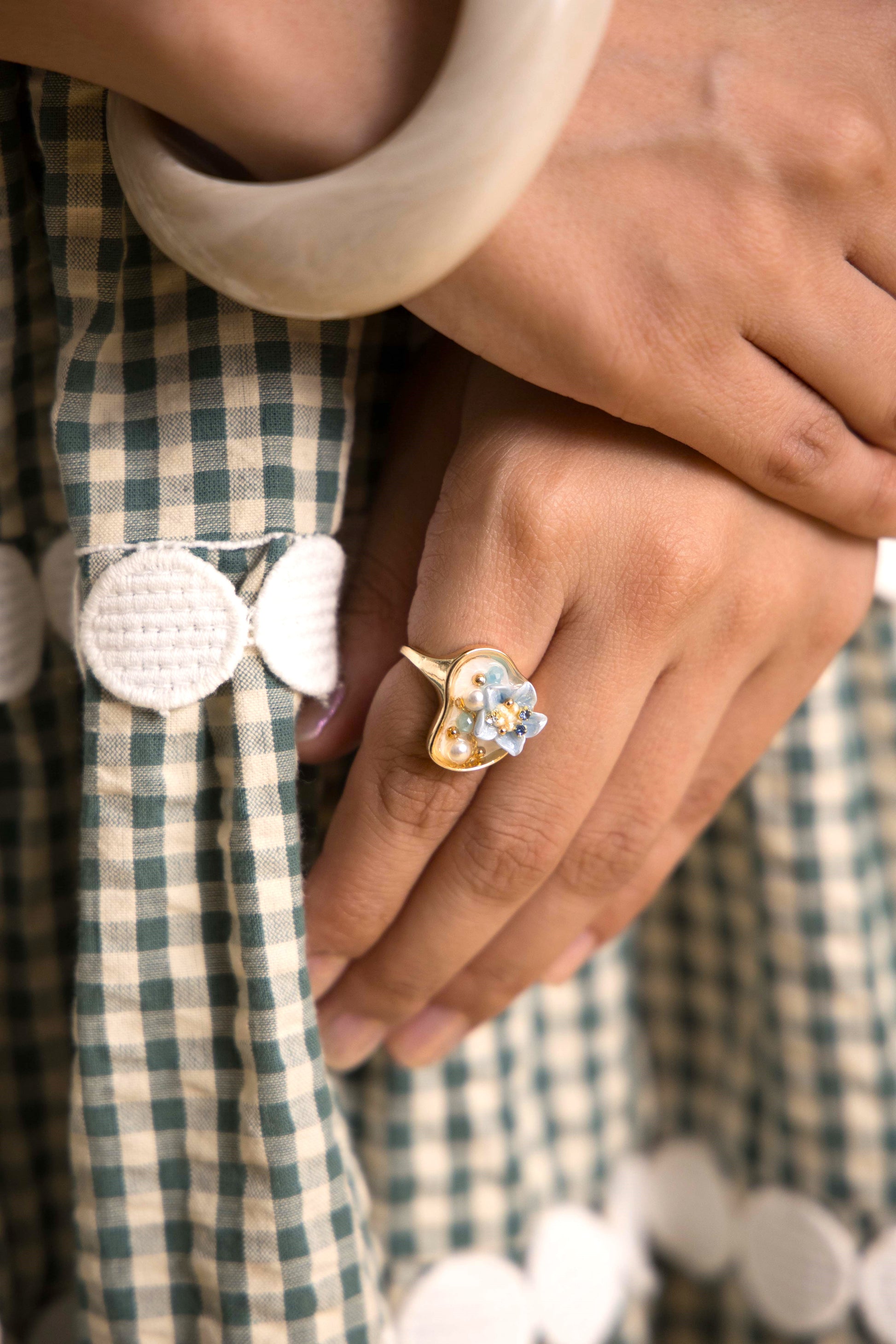 A gold-toned open band ring inspired by oceanic beauty, featuring a cluster of luminous pearls and a soft blue floral gem, arranged organically to resemble a hidden underwater treasure.