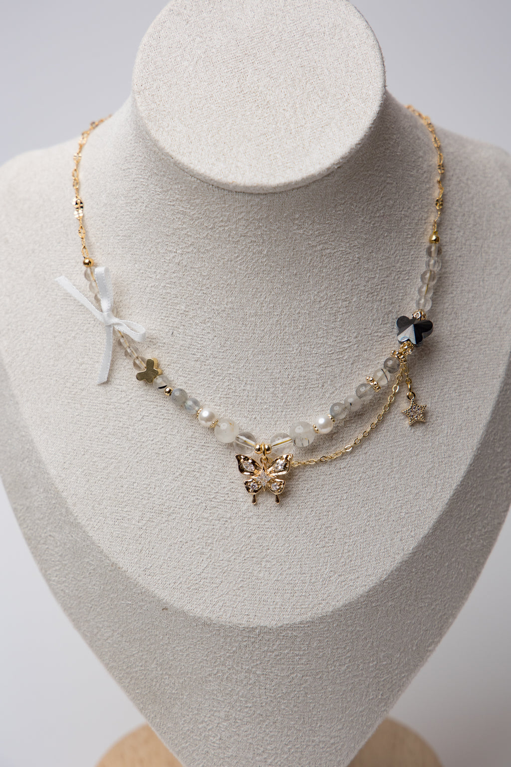 Layered Butterfly Charm Necklace with a two-layer chain featuring a crystal-studded butterfly, star charm, ribbon detail, and a small black bead for a whimsical, graceful look.