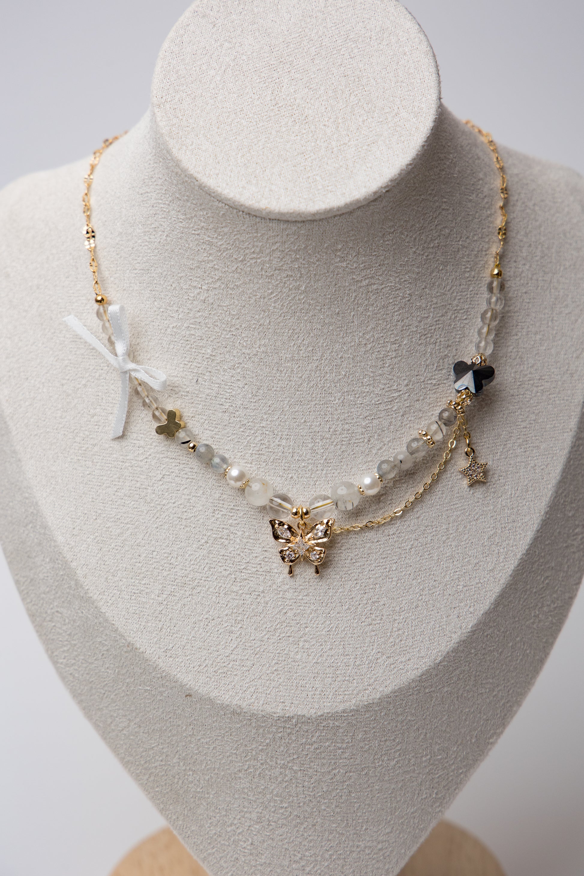 Layered Butterfly Charm Necklace with a two-layer chain featuring a crystal-studded butterfly, star charm, ribbon detail, and a small black bead for a whimsical, graceful look.