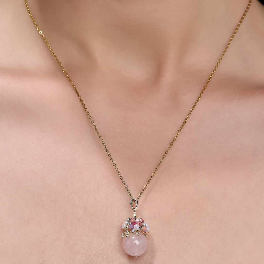 Close-up of an elegant necklace featuring a soft pink rose quartz orb, accented with a cluster of luminous freshwater pearls and deep pink tourmaline beads, evoking charm, femininity, and grace.