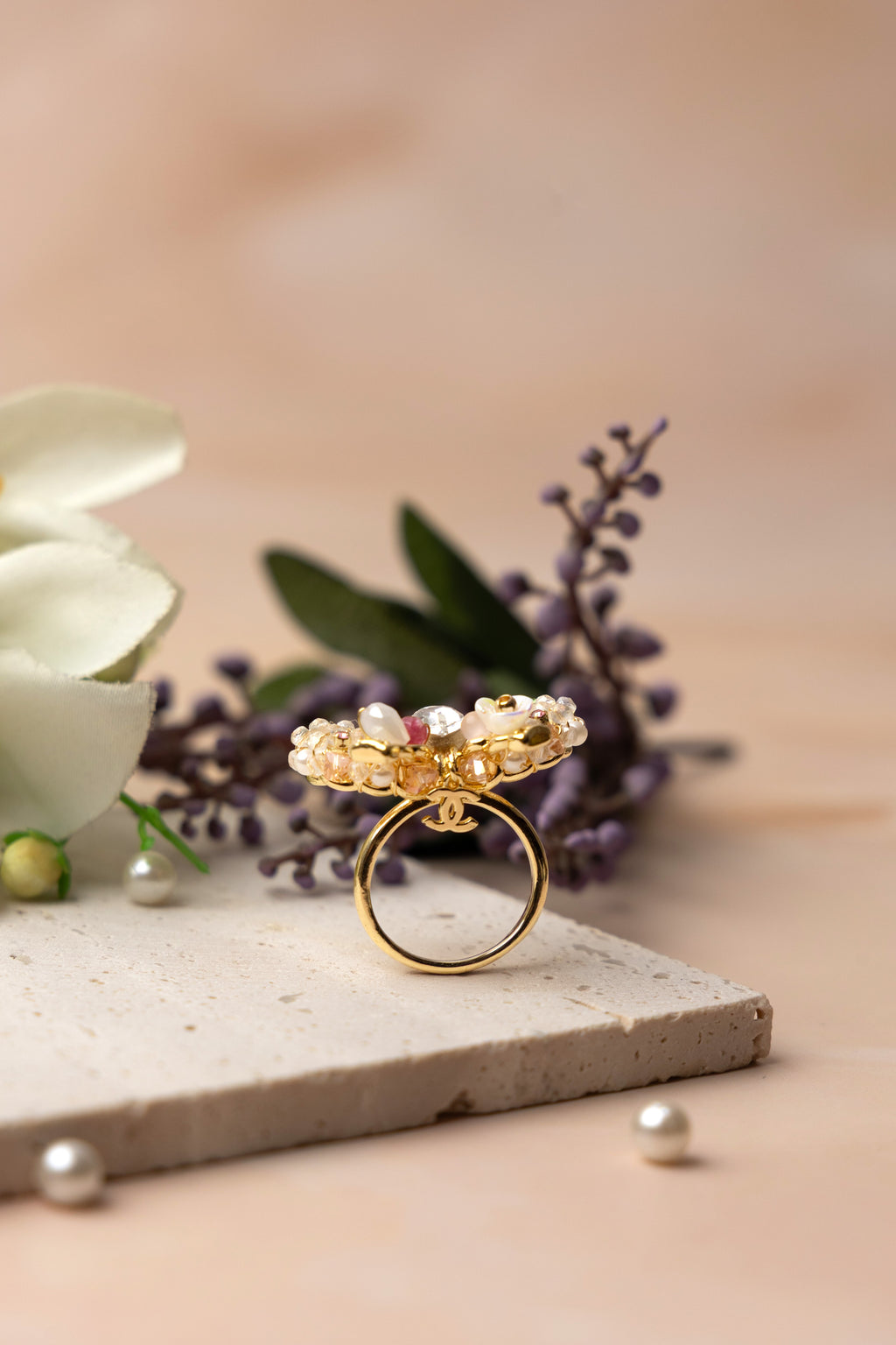 A delicately handcrafted gold-tone ring in the shape of a bow, adorned with clusters of luminous pearls, shimmering crystals, and soft pastel accents, showcasing feminine charm and exquisite artisanal detail.