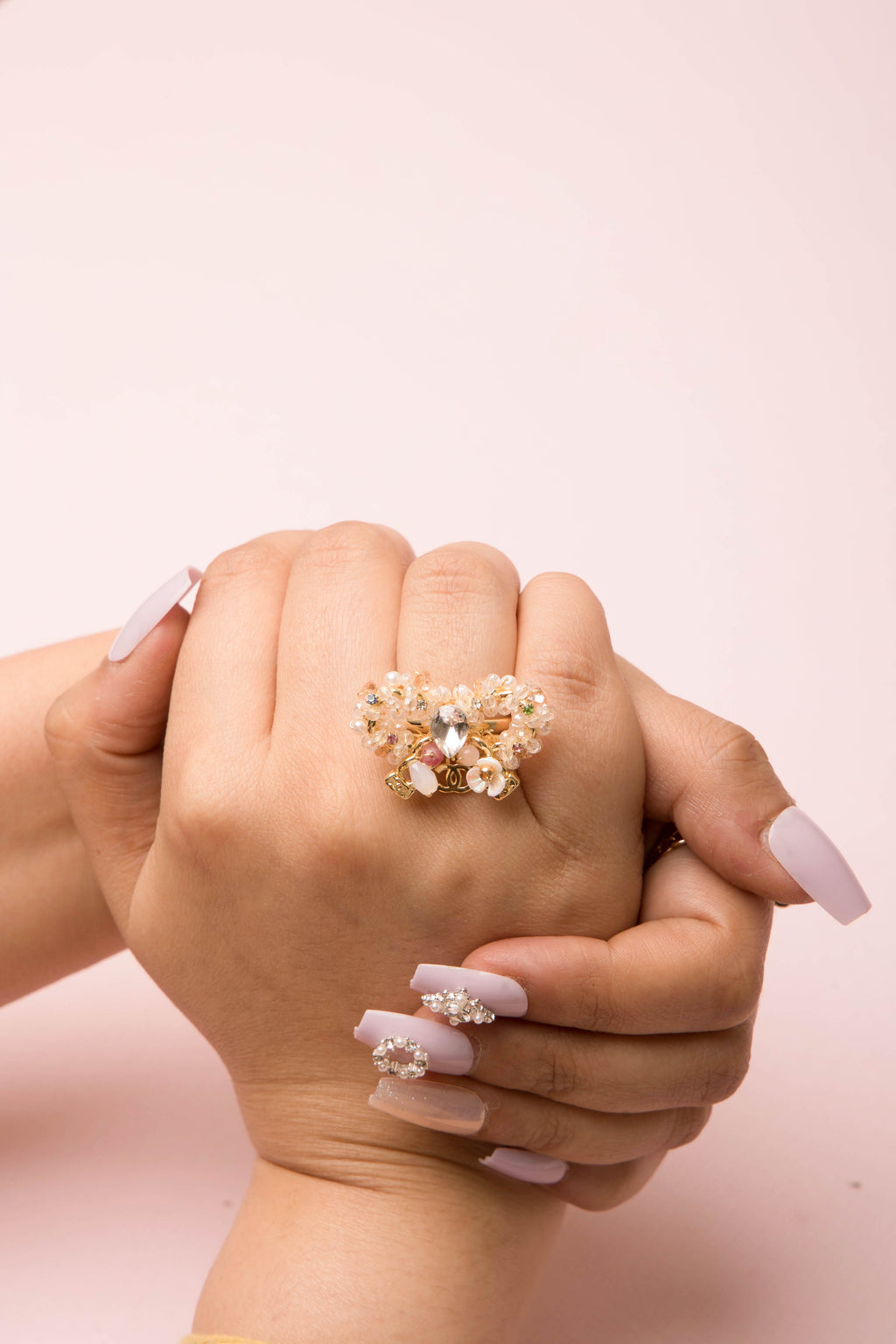 A delicately handcrafted gold-tone ring in the shape of a bow, adorned with clusters of luminous pearls, shimmering crystals, and soft pastel accents, showcasing feminine charm and exquisite artisanal detail.