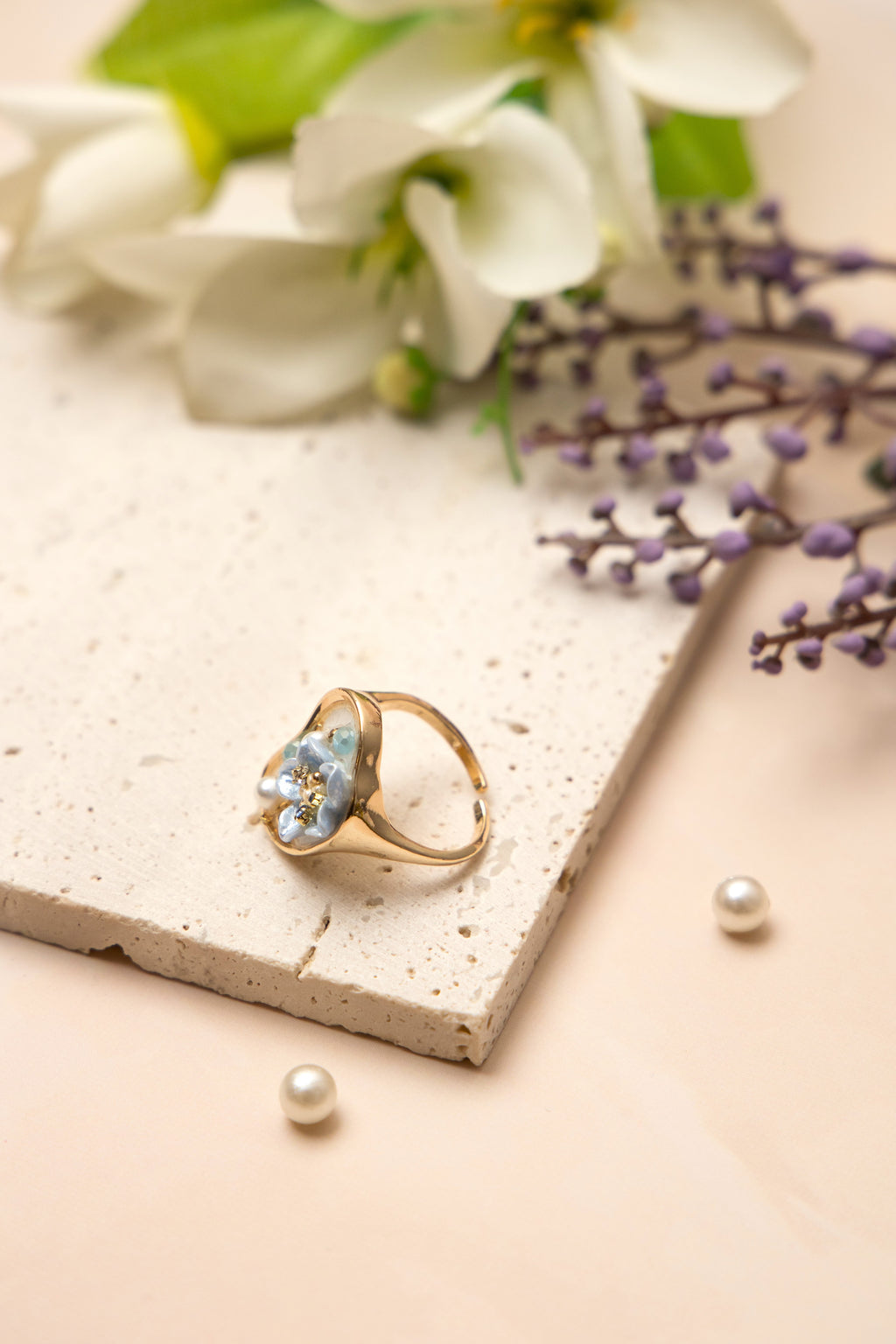 A gold-toned open band ring inspired by oceanic beauty, featuring a cluster of luminous pearls and a soft blue floral gem, arranged organically to resemble a hidden underwater treasure.
